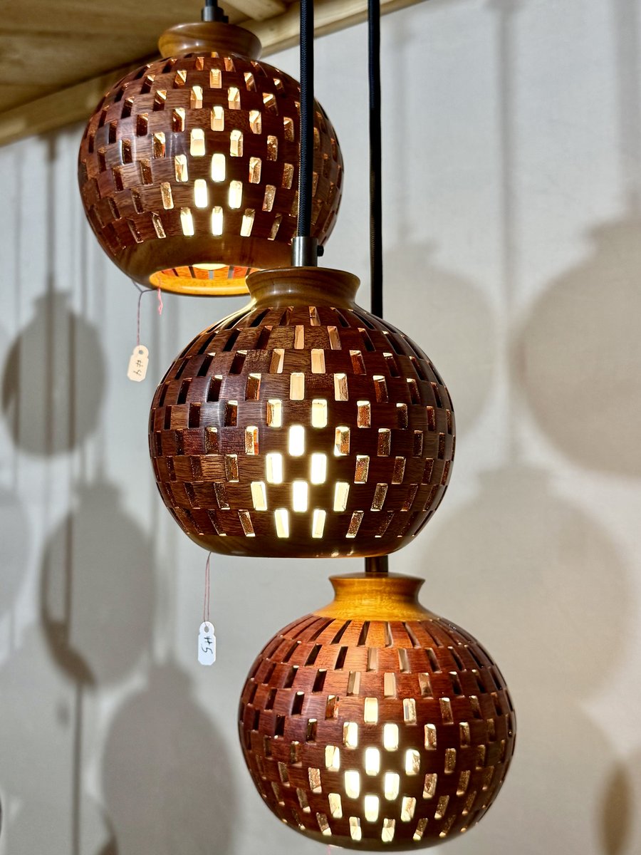 Angled view of a three-globe handmade bloodwood and canarywood pendant chandelier showing staggered cascade and warm glow