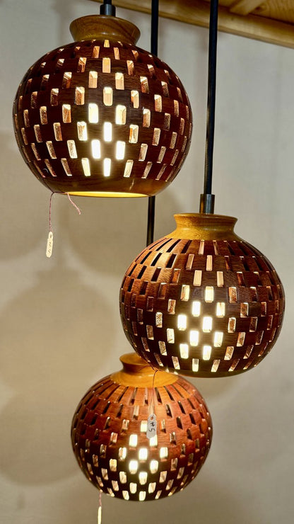 Second angle of a three-globe handmade bloodwood and canarywood pendant chandelier highlighting rich wood texture and warm light