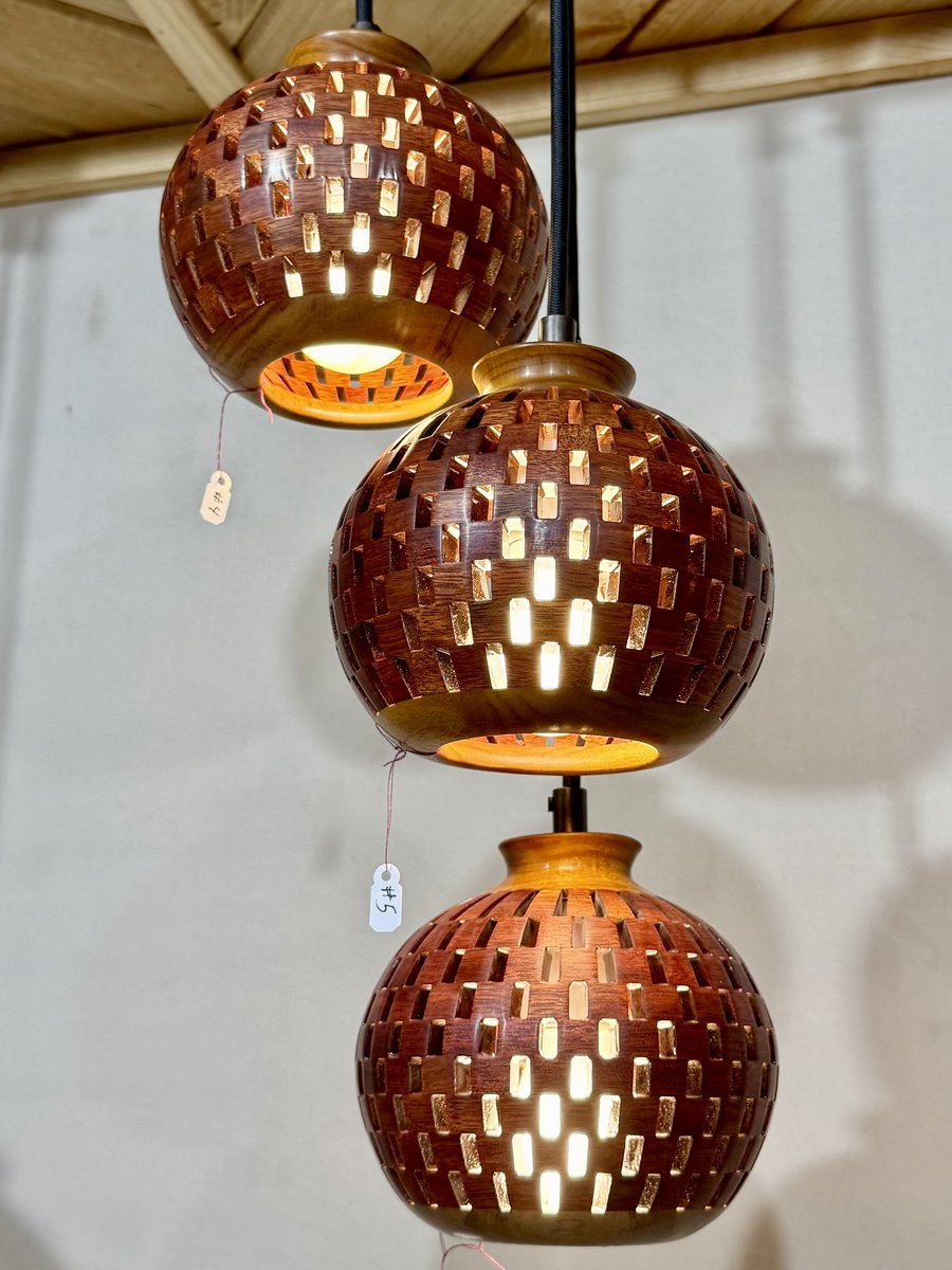 Close-up of a three-globe handmade bloodwood and canarywood pendant chandelier showing basket-weave cutouts and warm amber glow