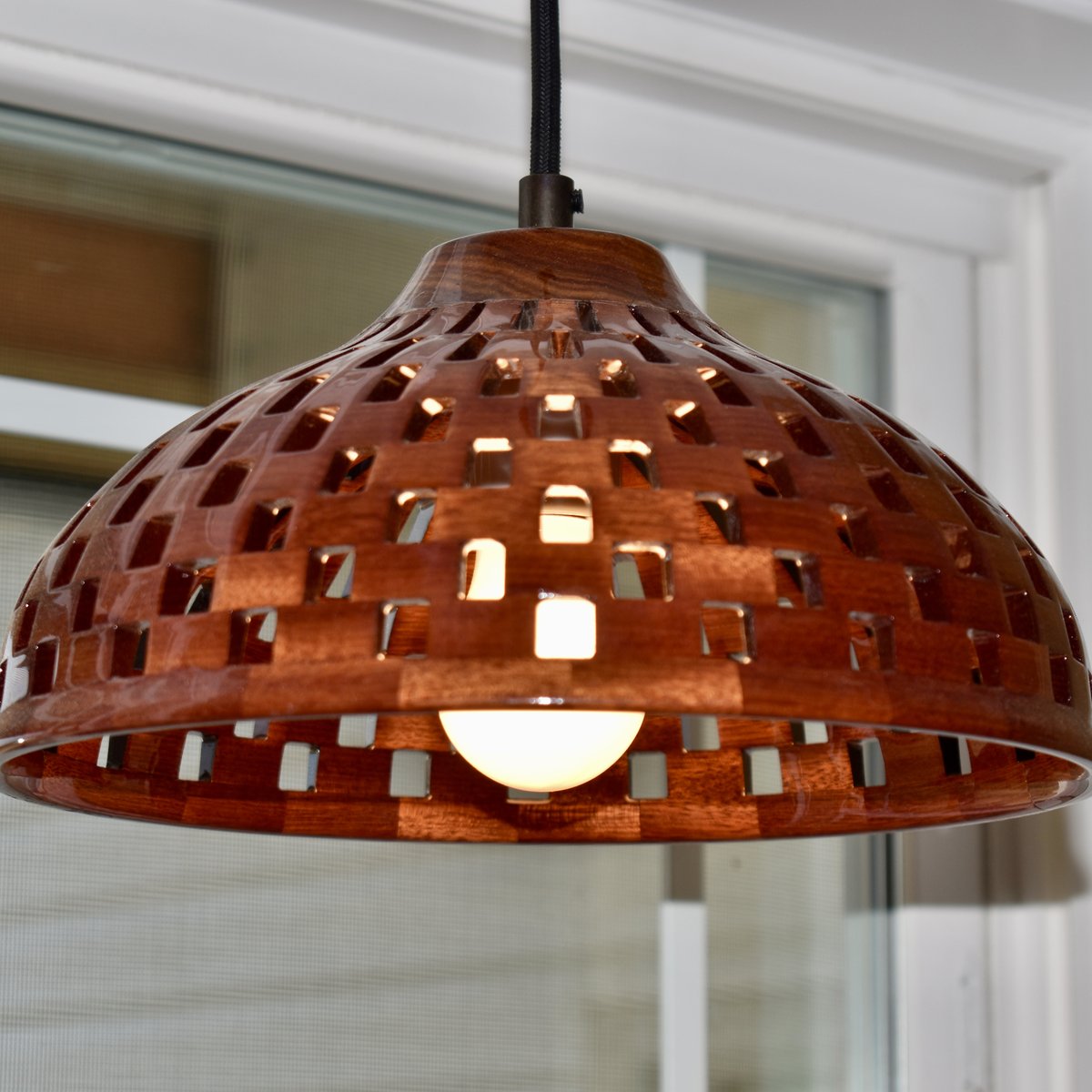 Lit handmade bloodwood dome pendant light viewed from below, showing warm glow radiating through lattice cutouts