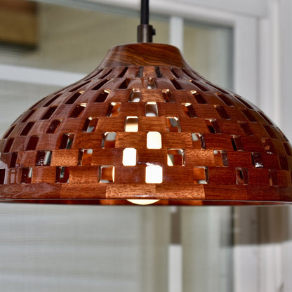 Close-up detail of a handmade bloodwood dome pendant light showing basket-weave cutout pattern and vibrant red grain