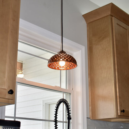 Handmade bloodwood dome pendant light installed above a kitchen sink, glowing warmly between maple cabinets