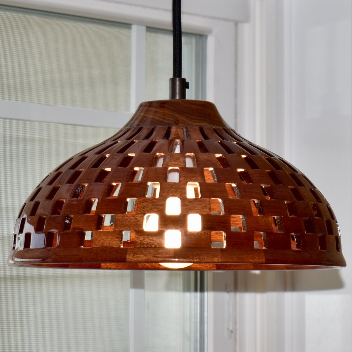 Side view of a handmade bloodwood dome pendant light with basket-weave cutout pattern and rich red wood grain