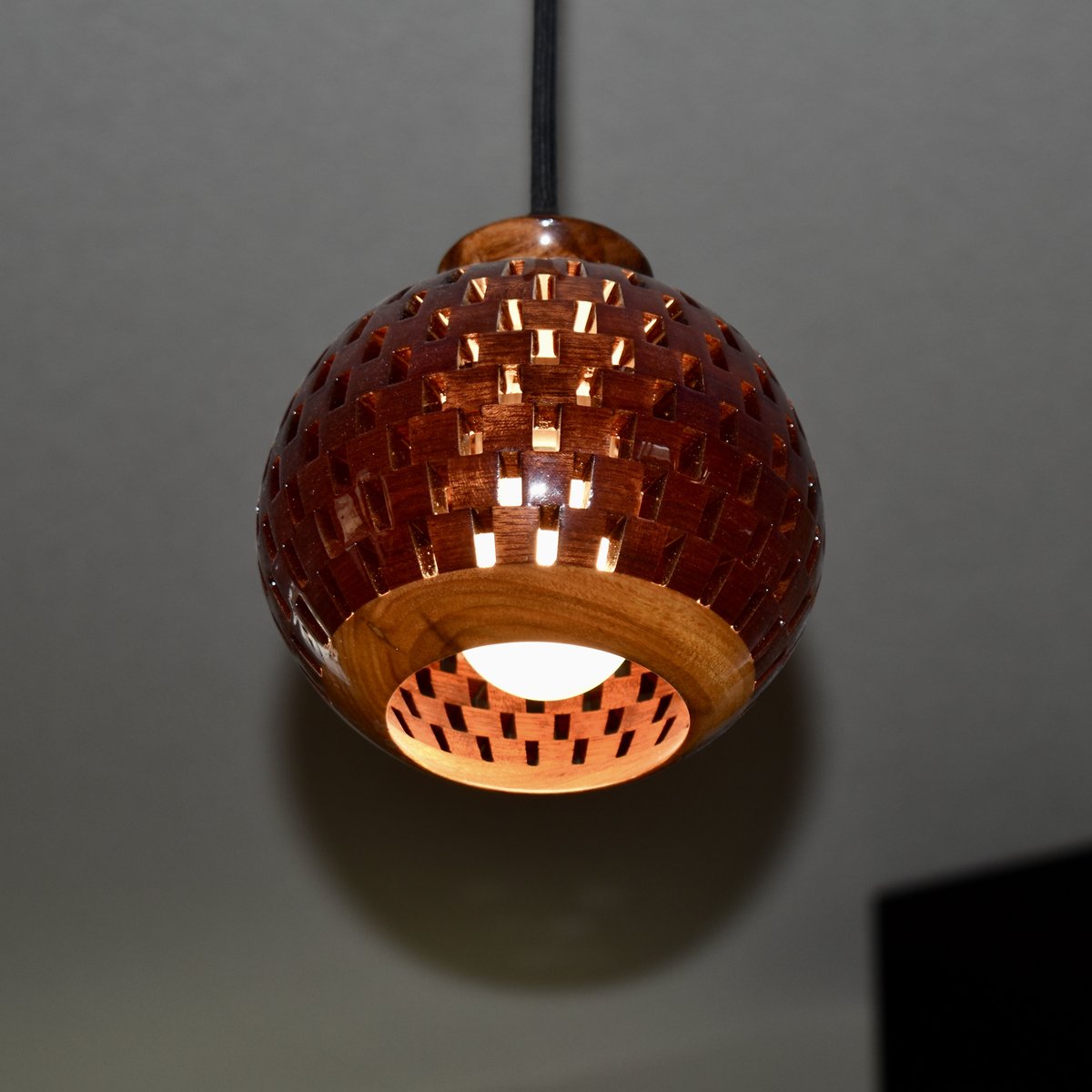 Handmade bloodwood globe pendant light against a dark background, highlighting the spherical open-segment design