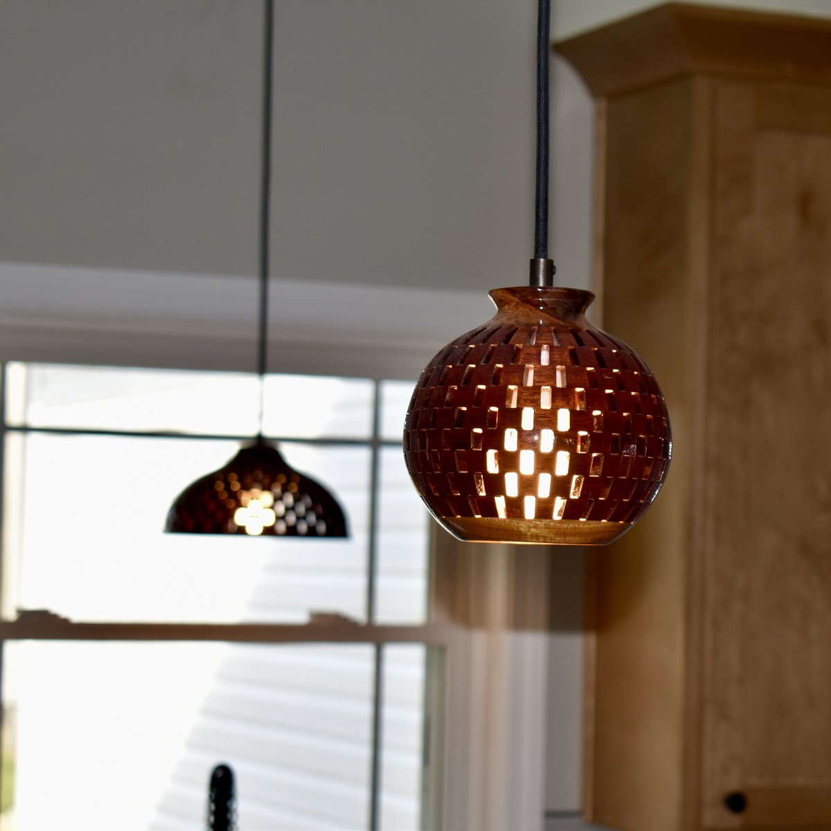 Close-up of a handmade bloodwood globe pendant light installed in a kitchen, warm light glowing through segment gaps