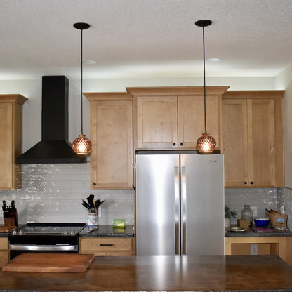 Pair of handmade bloodwood globe pendant lights hanging in a modern kitchen with stainless refrigerator and maple cabinets